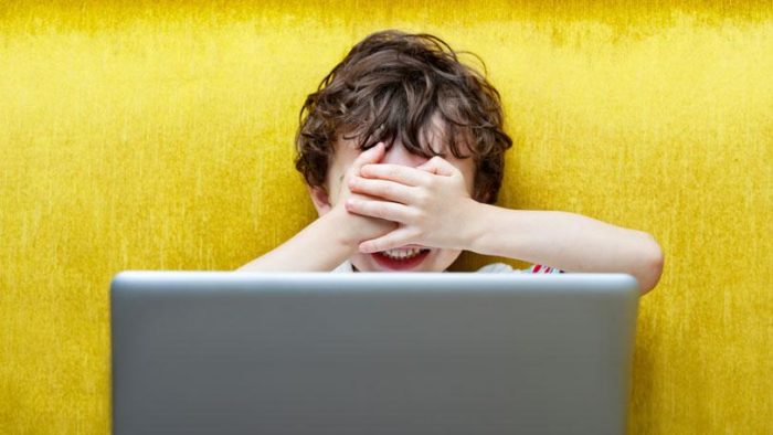 Boy covers his eyes in front of a laptop