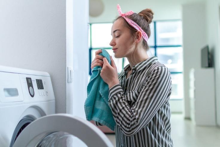 Mujer oliendo una toalla frente a la lavadora