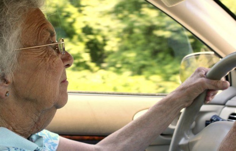 Anciana con lentes manejando con las manos en el volante