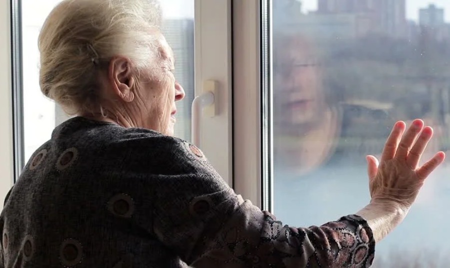 Anciana viendo a través del vidrio de la puerta y tocándola