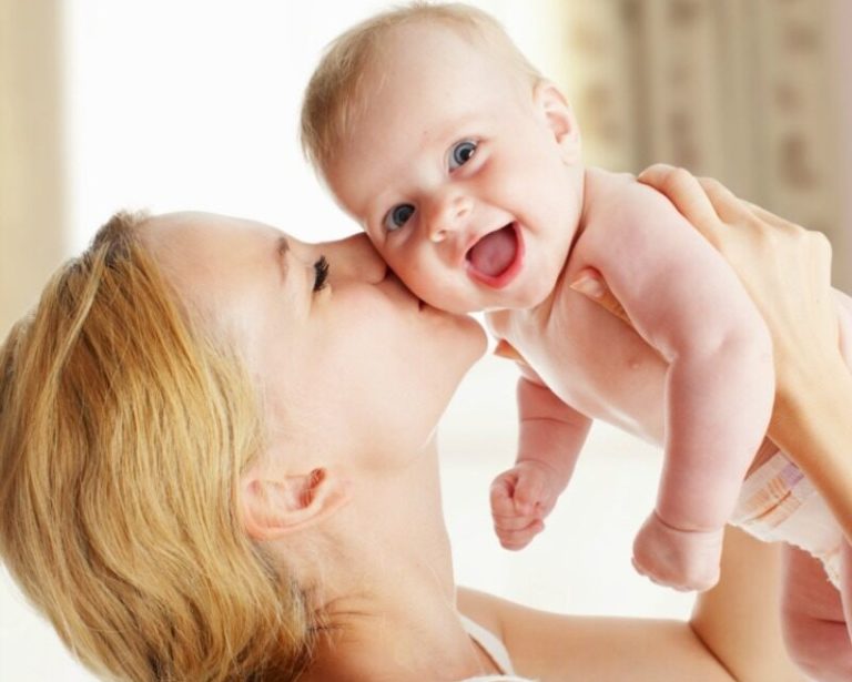 Mujer cargando y besando en la mejilla a un bebé sonriendo